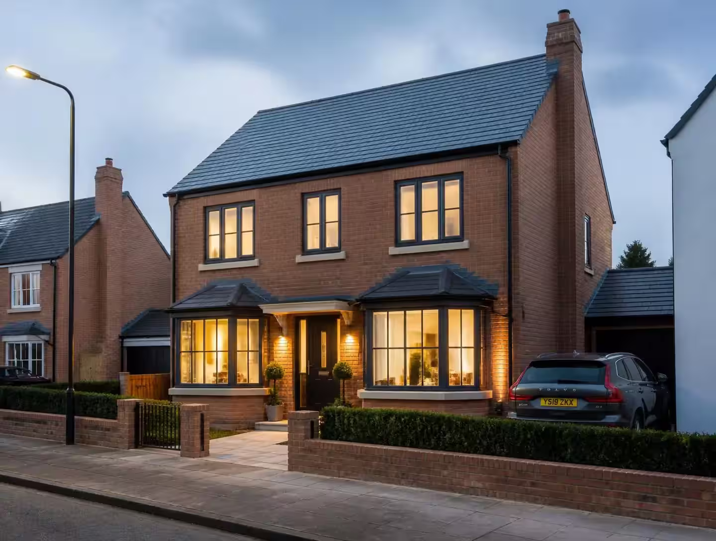Modern red brick and dark-clad British home lit at dusk